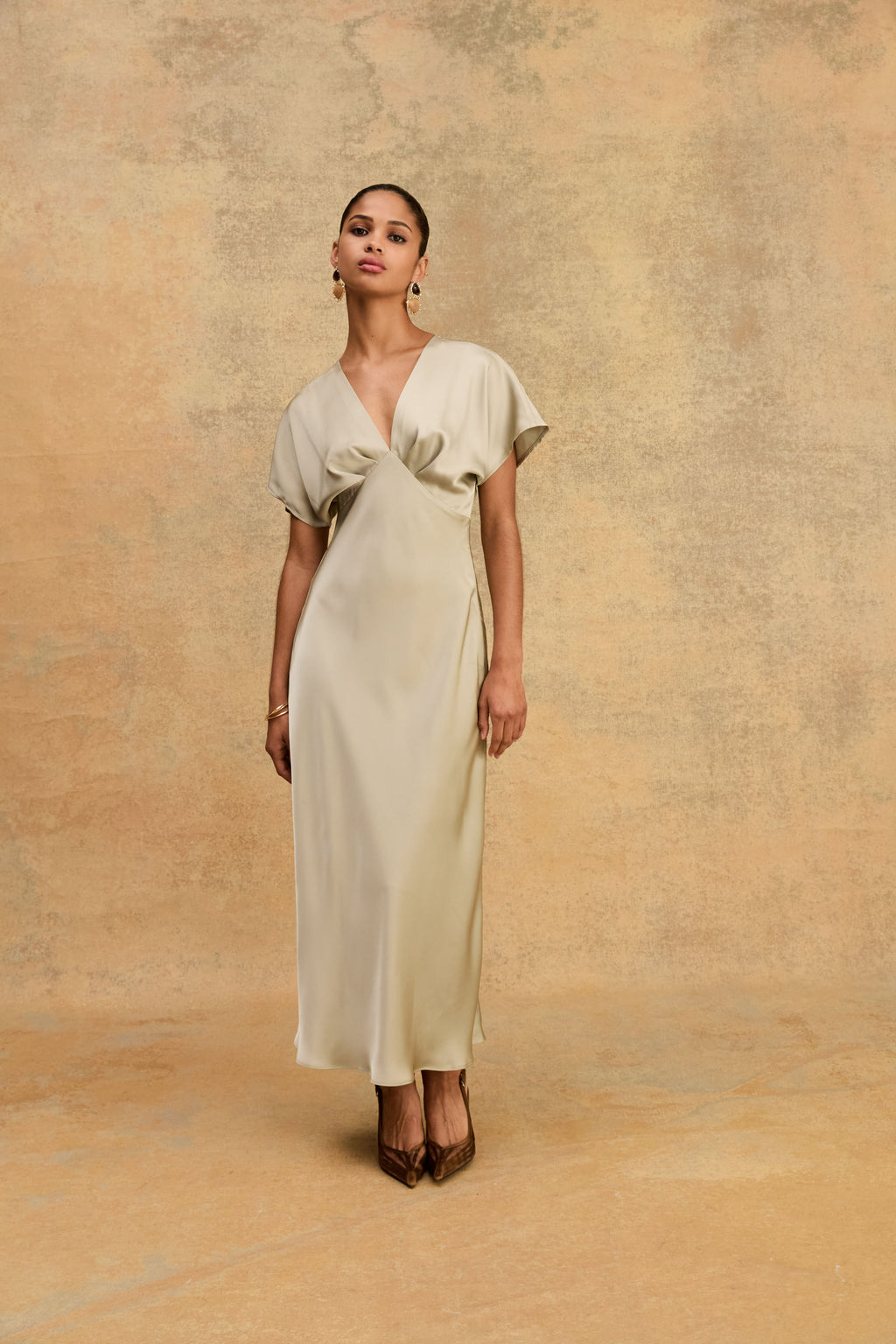 Front view of the sage Catalina V-Neck Satin Dress against a warm beige wall