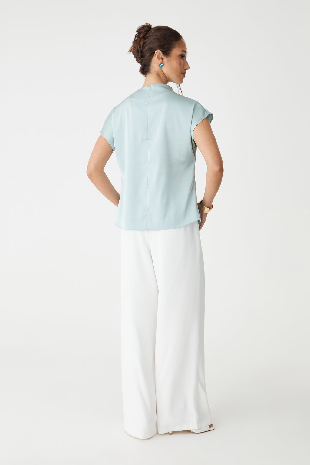 Back view of the pale blue Zafina Pleated Draped Top with invisible back zipper, worn with white trousers