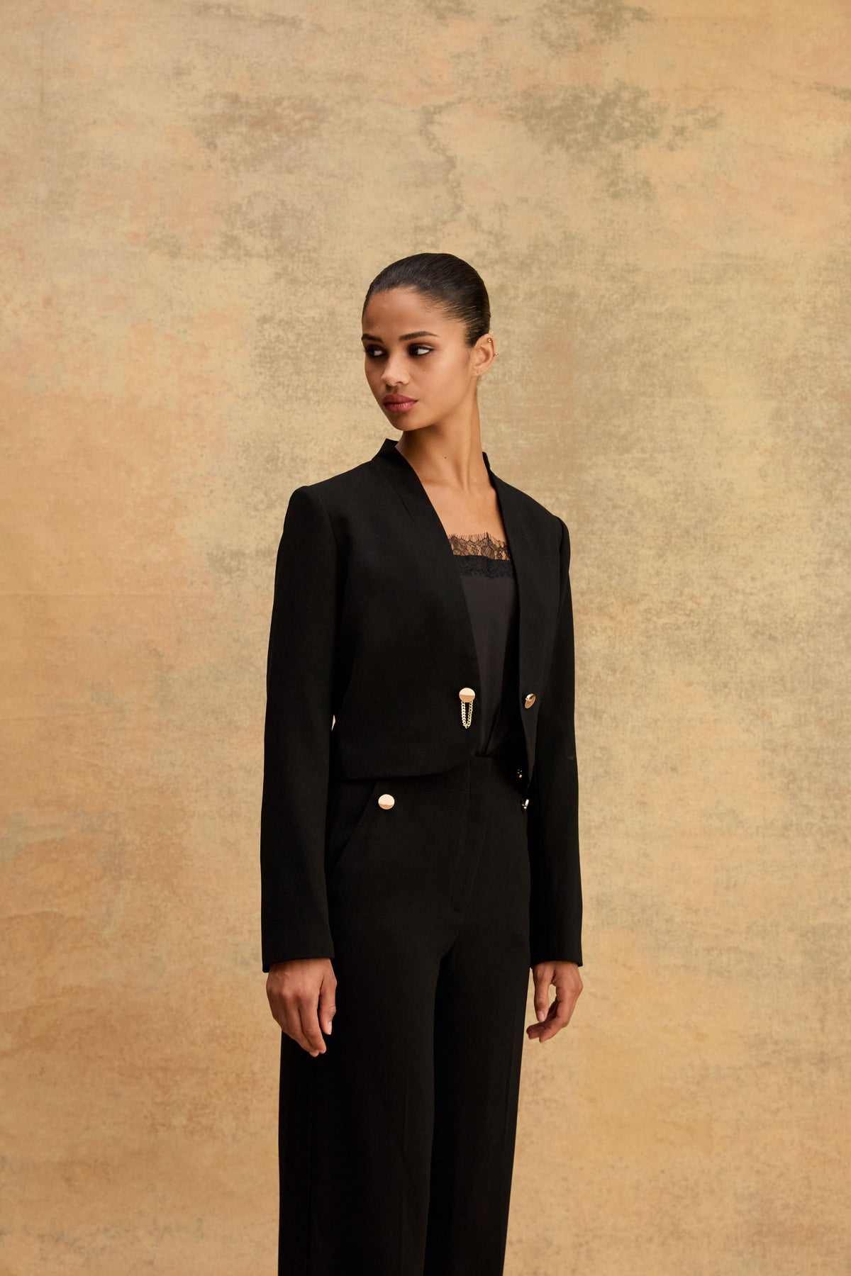 Side view of the black cropped jacket showing gold-tone clasp and curved hemline