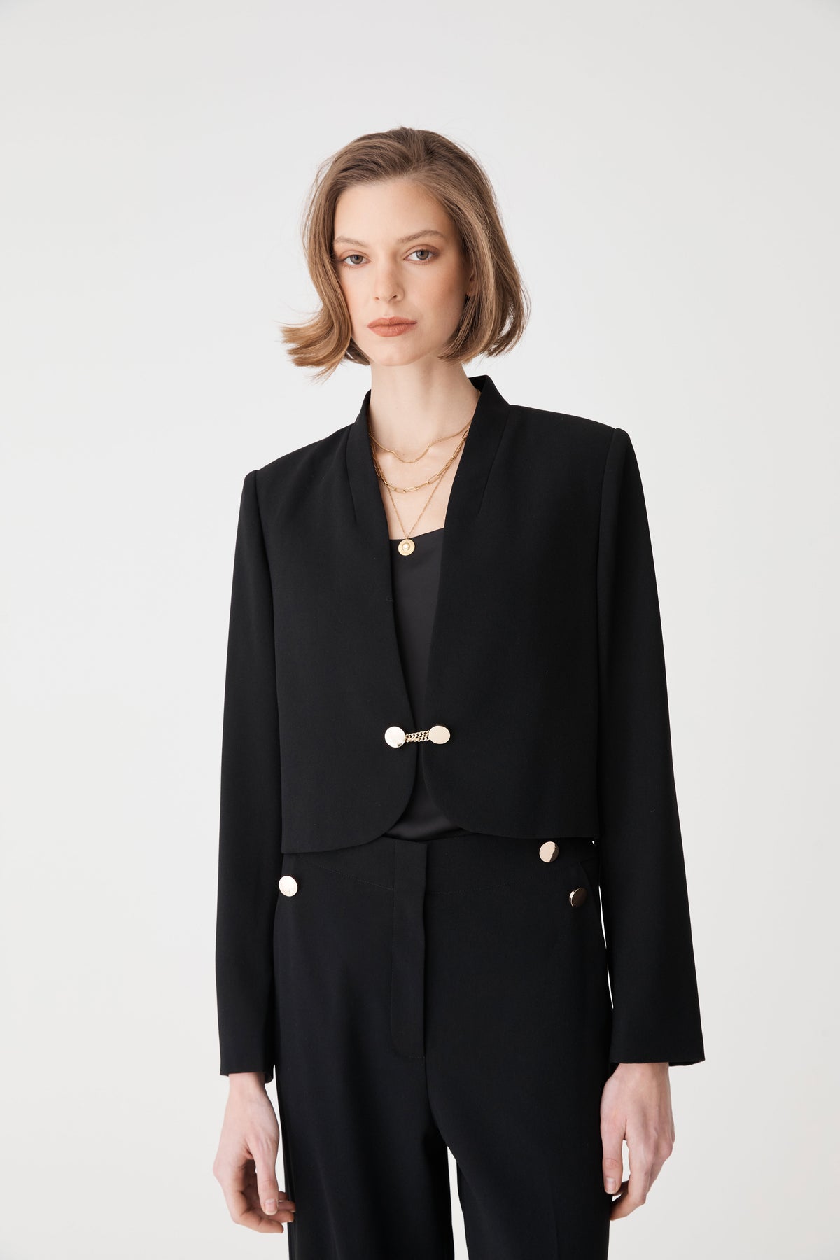 Front close-up of the black cropped jacket with long straight sleeves and chain-link necklace