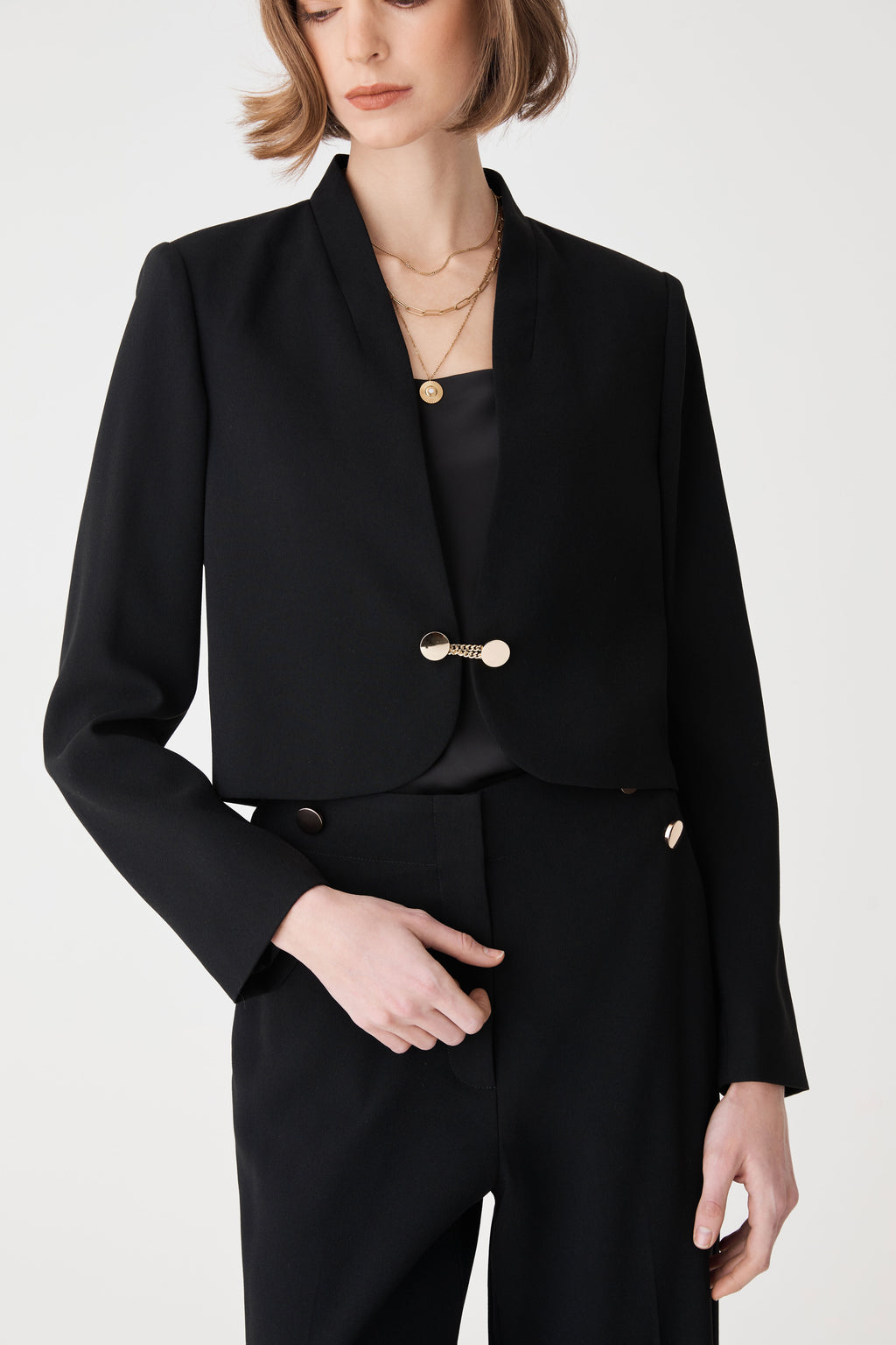 Close-up of the black jacket's collarless V neckline and gold dual-disc clasp