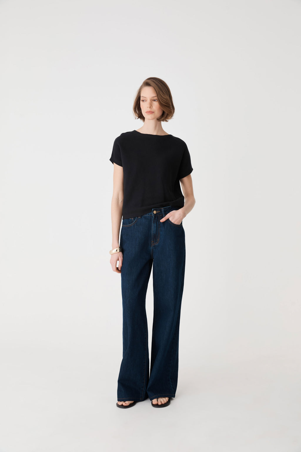 Front view of the black knit top tucked into dark blue wide-leg jeans