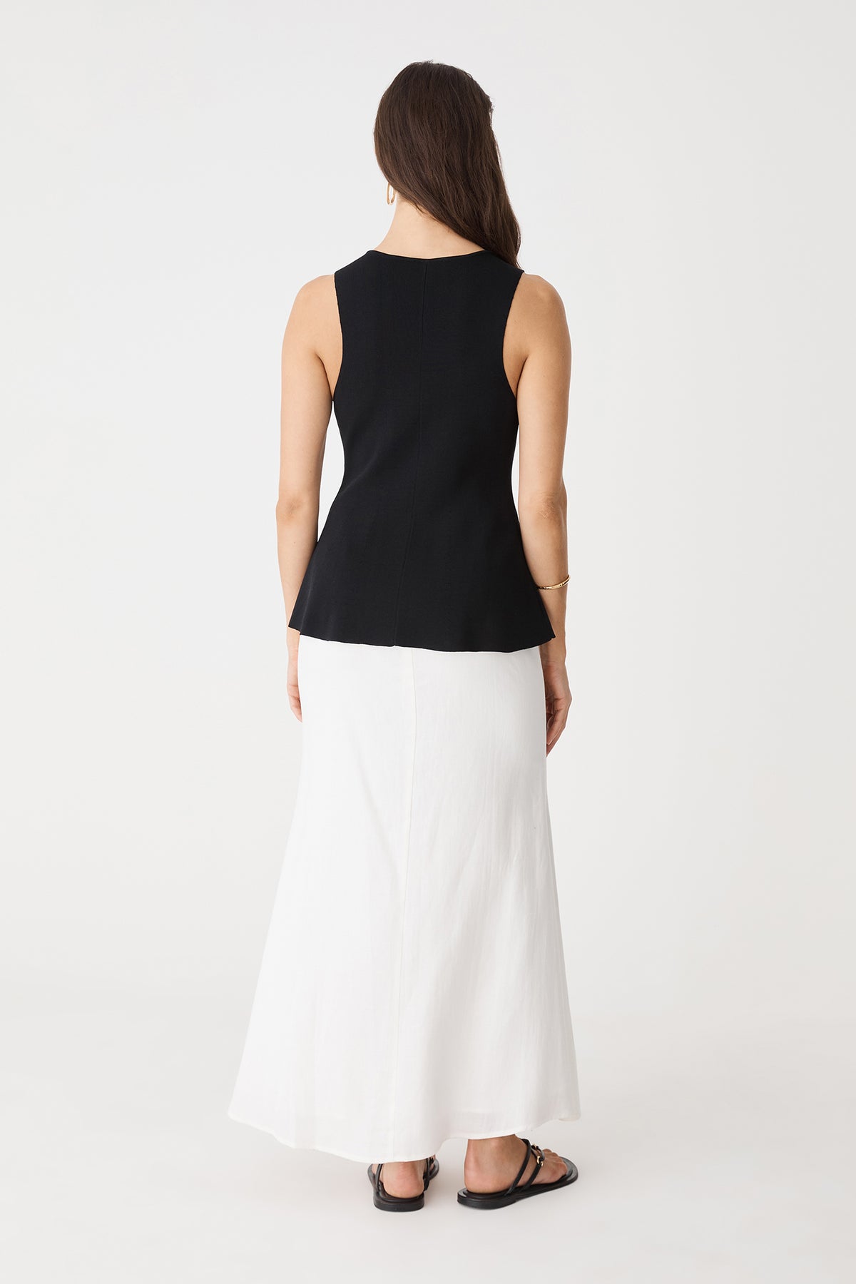 Back view of the black Valerie Button Peplum Knit Top worn with a white maxi skirt