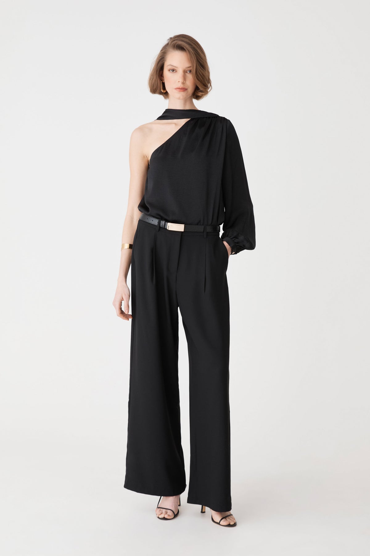 Daphne Pleated Crepe Pants in black, front view, worn with a black one-shoulder top and belt