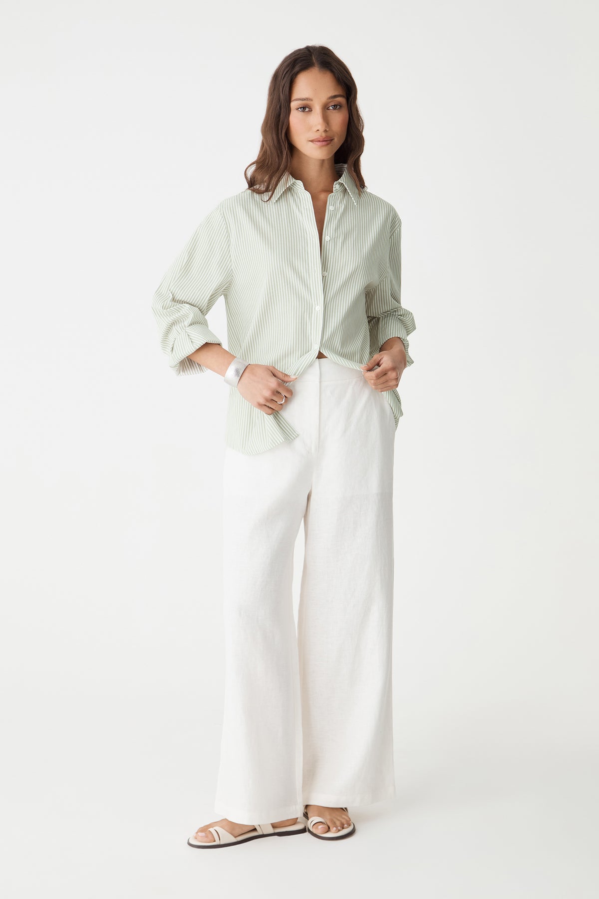 Front view of the green stripe shirt with sleeves pushed up, worn with white trousers