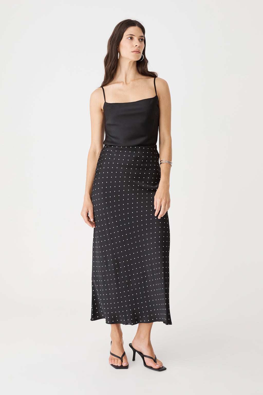 Front view of the black and white dot bias-cut midi skirt worn with a black camisole
