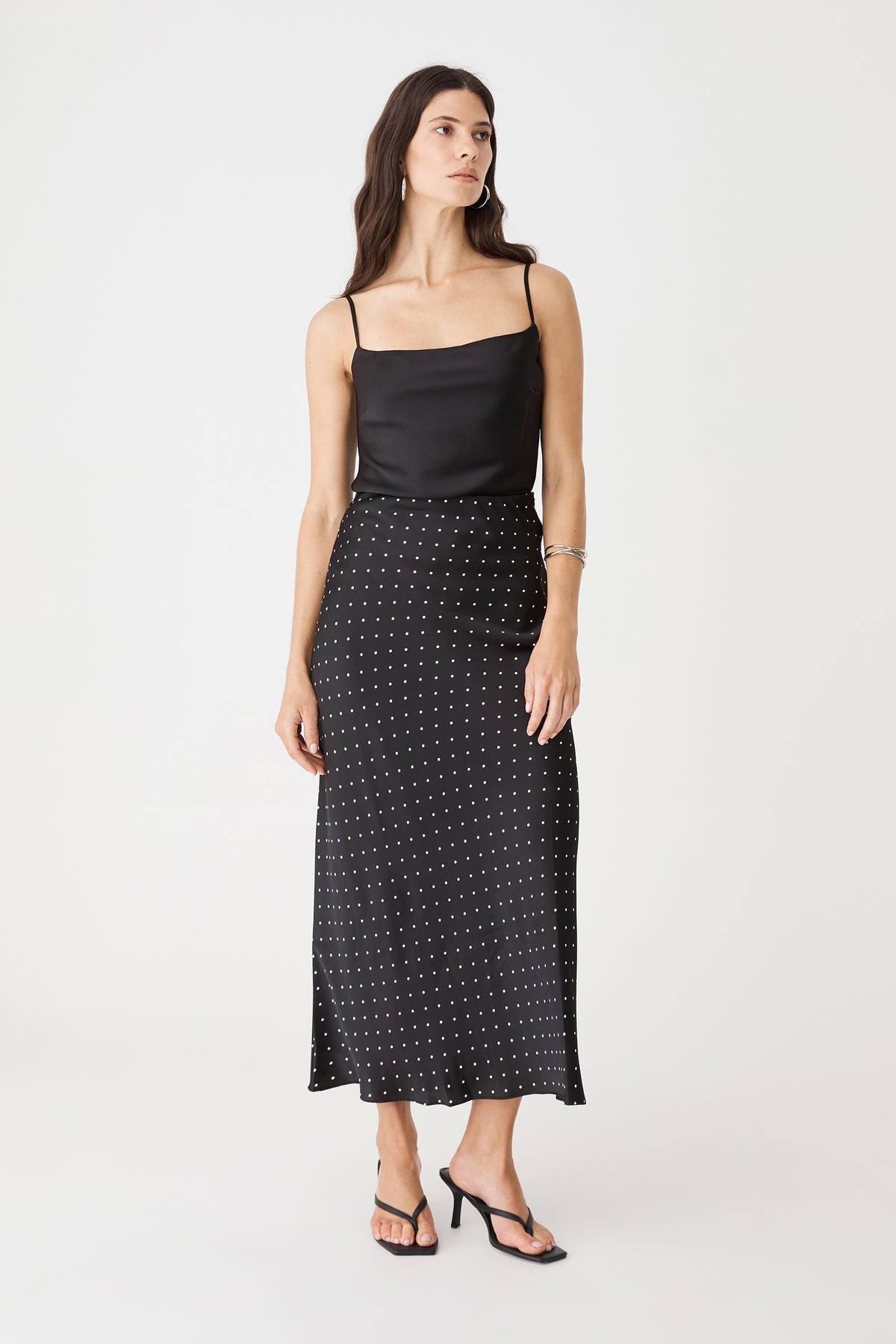 Front view of the black and white dot bias-cut midi skirt worn with a black camisole