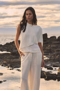 Cecilia Asymmetric Top in ivory worn with ivory wide-leg trousers, front view outdoors by the sea